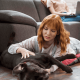 Dog lying on floor with woman petting her, indoor scene, cozy home environment.