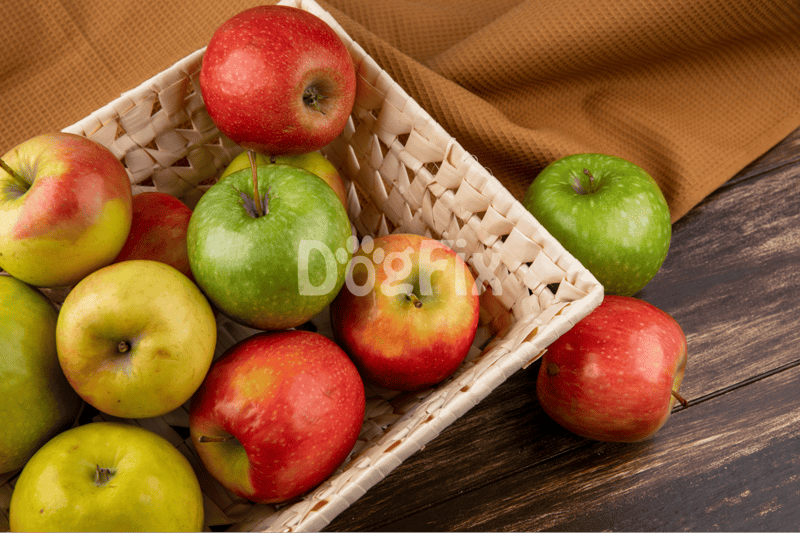 Colorful red and green apples in a woven basket on rustic wood table, ideal for dog nutrition and healthy treats.