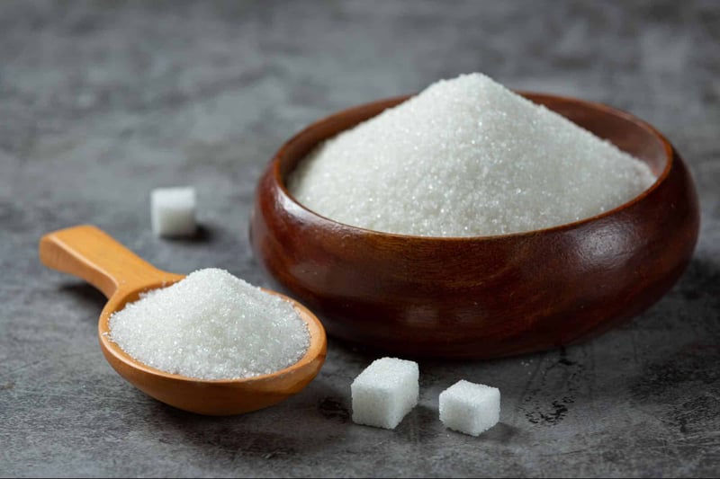 Alt text: Wooden bowl filled with white granulated sugar with sugar cubes and scoop nearby.