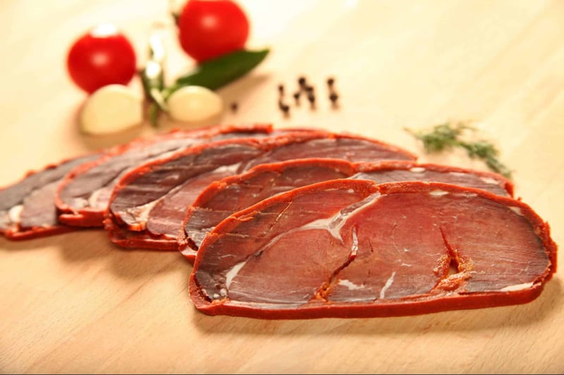 Tasty assorted meat slices including beef, turkey, and ham with herbs and vegetables on a wooden background.