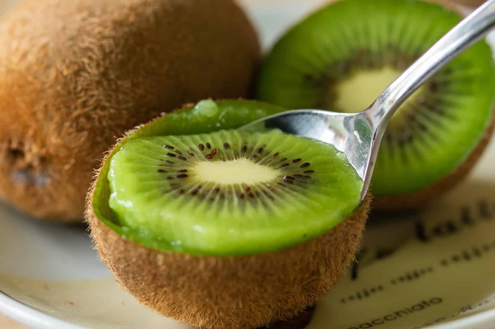 Close-up of sliced kiwi with spoon, showcasing vibrant green flesh and tiny black seeds.