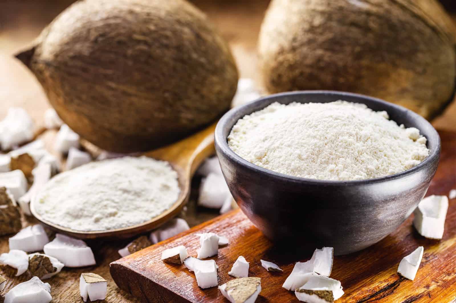 A bowl of coconut flour surrounded by whole coconuts and coconut pieces, ideal for healthy dog treats and recipes.