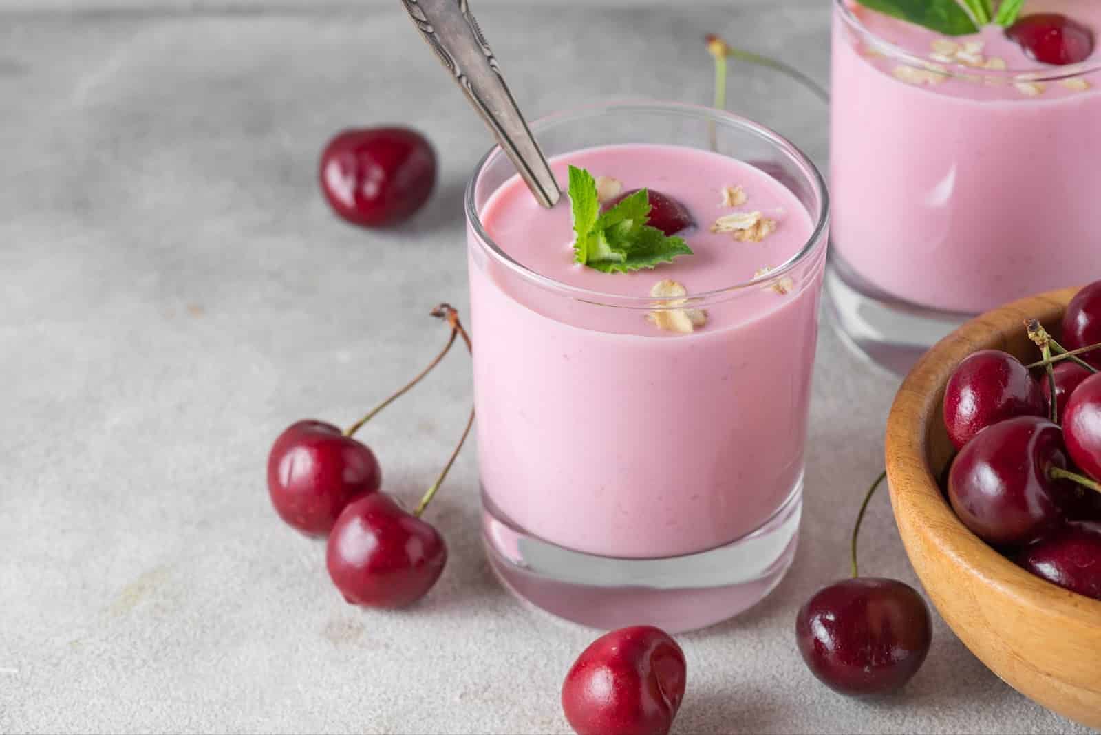 Delicious pink cherry yogurt smoothie in a glass with fresh cherries and mint, perfect for healthy summer refreshment.