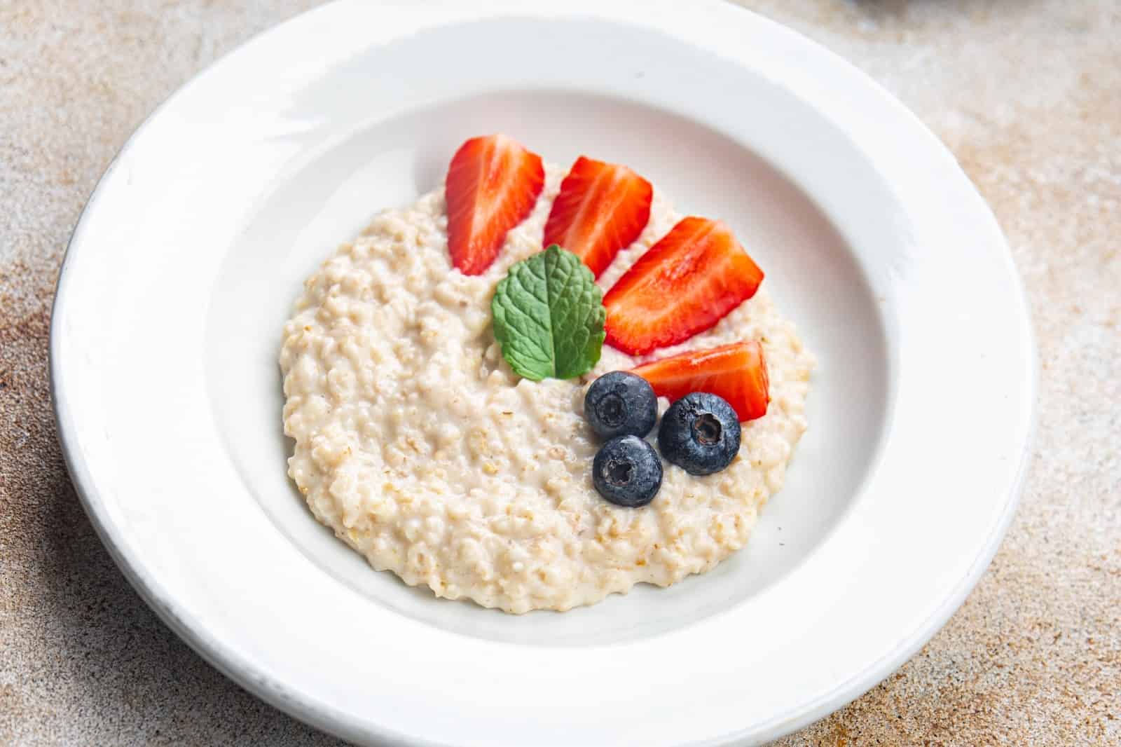 Oatmeal with strawberries, blueberries, and mint on a white plate, healthy dog-friendly breakfast.