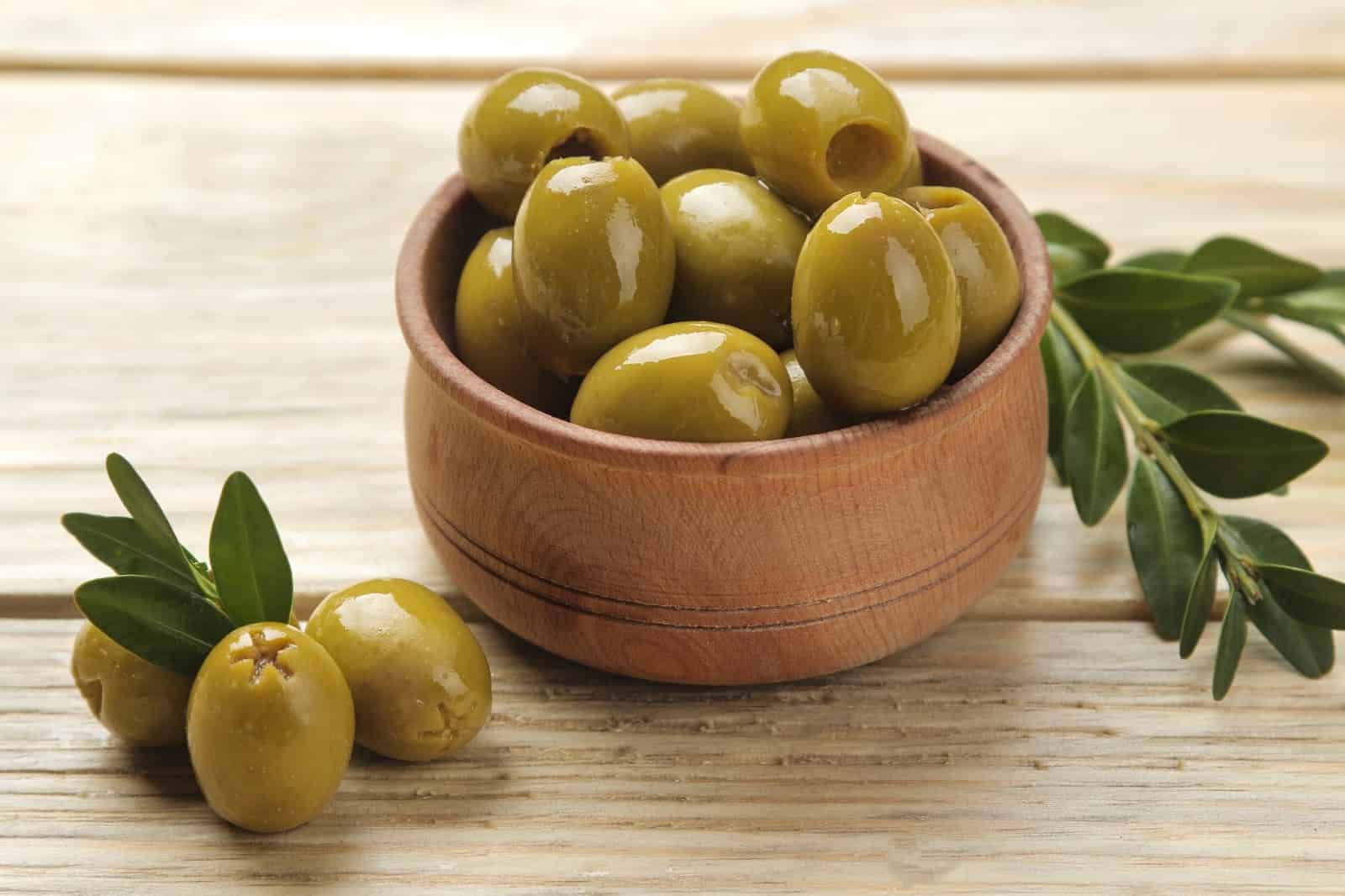 Bright green olives in a wooden bowl with fresh leaves, perfect for dog treats and healthy snacks.