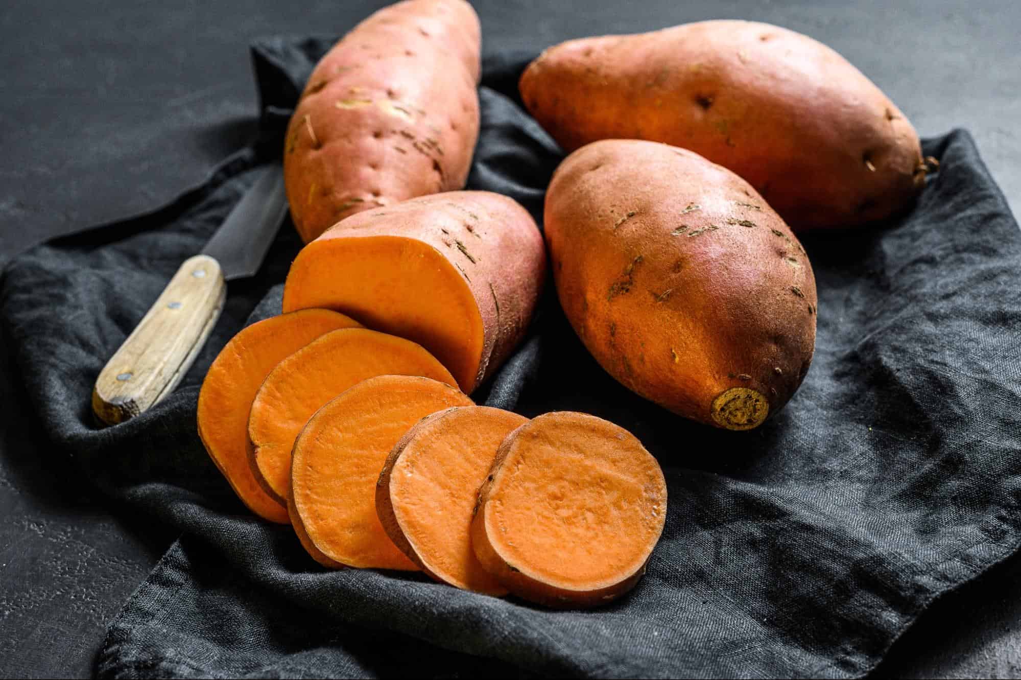 Fresh sweet potatoes on a black cloth with a knife for pet-friendly nutrition.