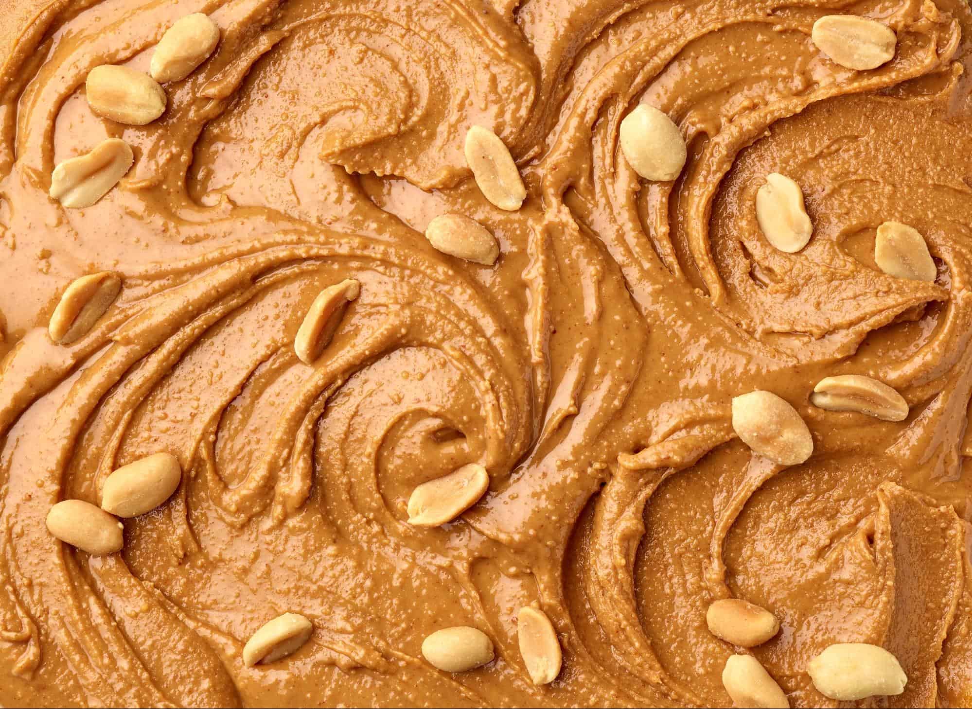 Close-up of caramel peanut spread, creamy and smooth with scattered peanuts.