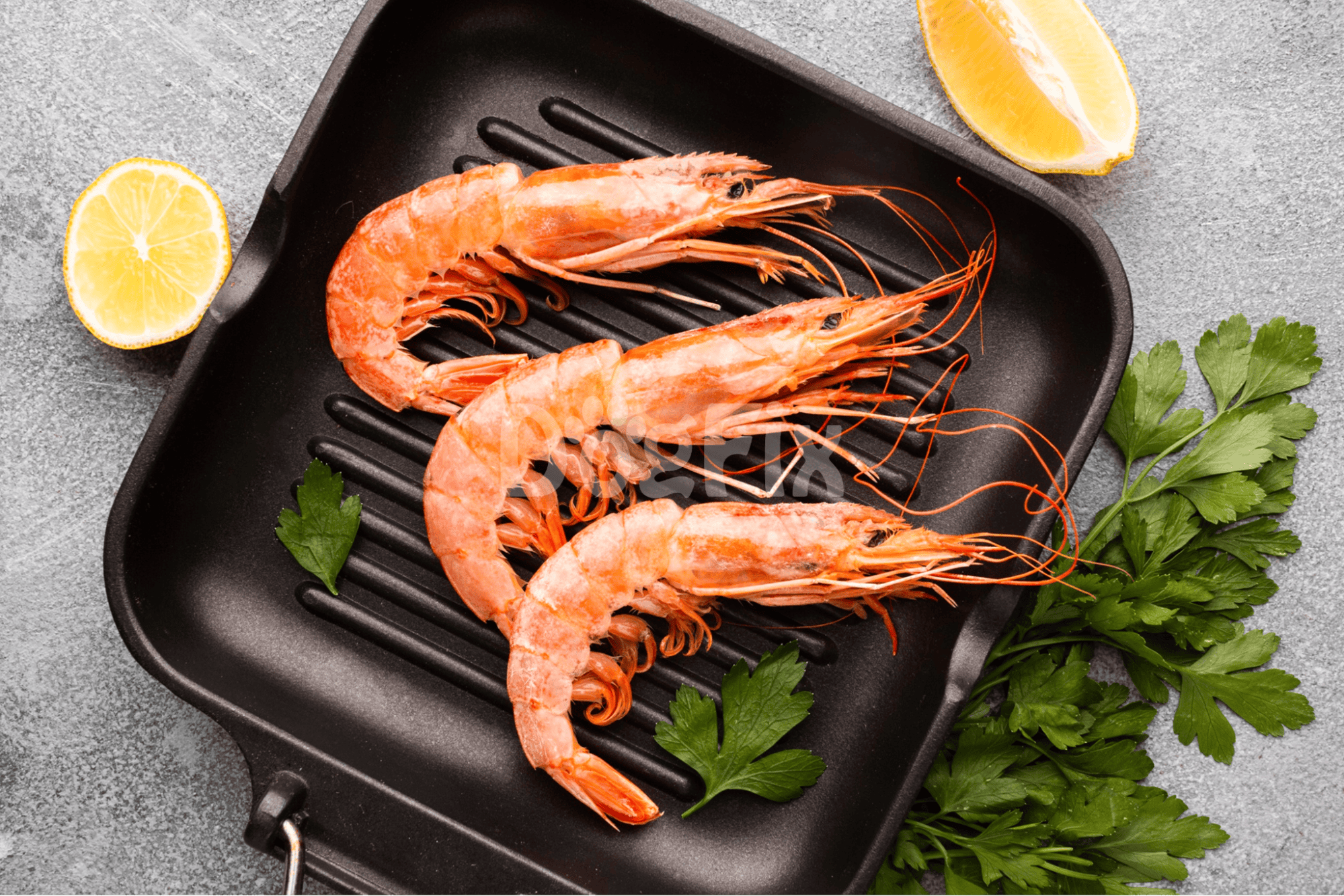 Fresh grilled shrimp served with lemon wedges and parsley on a griddle. Perfect seafood meal for dinner or lunch.