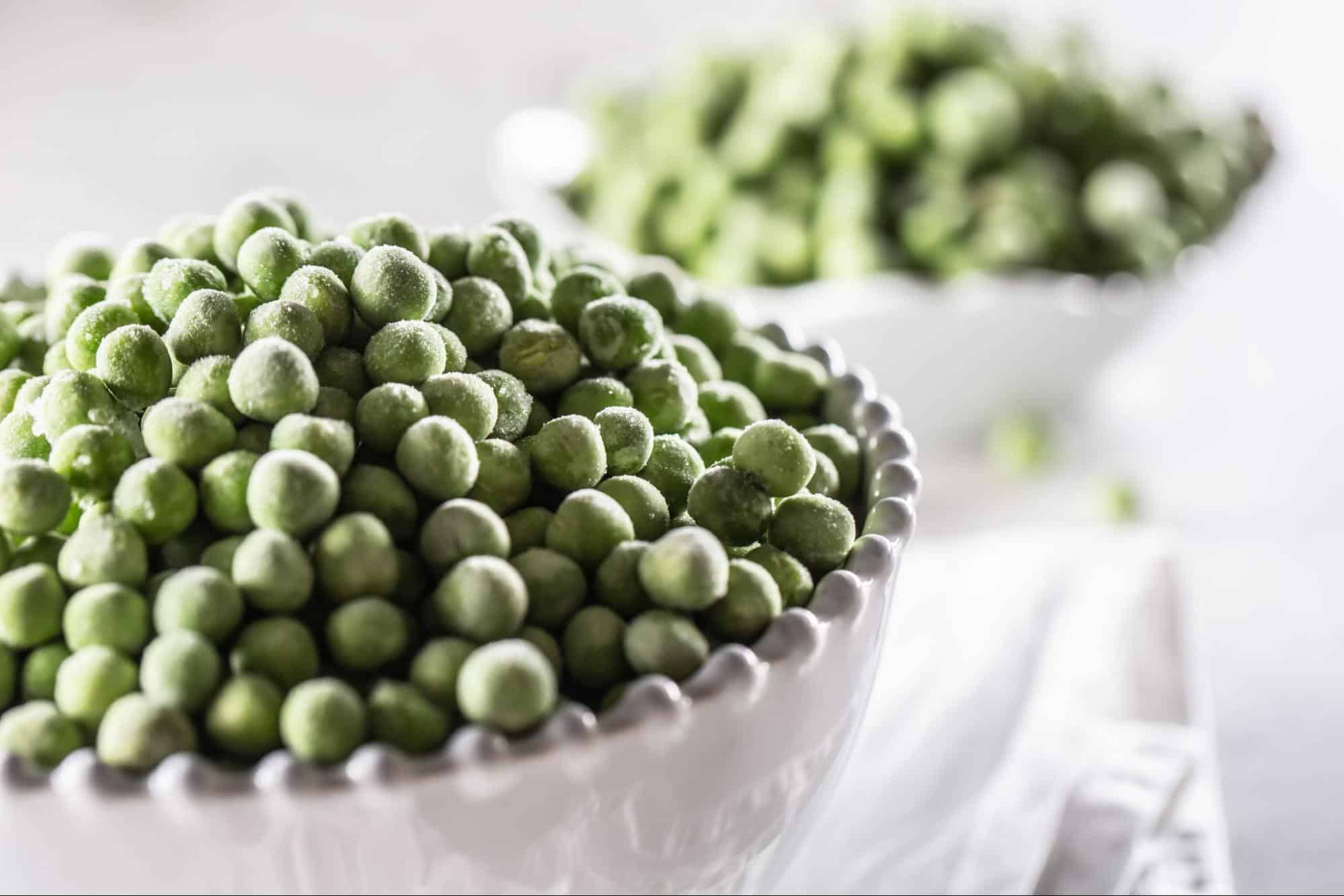 Close-up of frozen green peas in a white bowl, healthy vegetable snack, farm-fresh, vegetarian food, natural produce, organic peas.