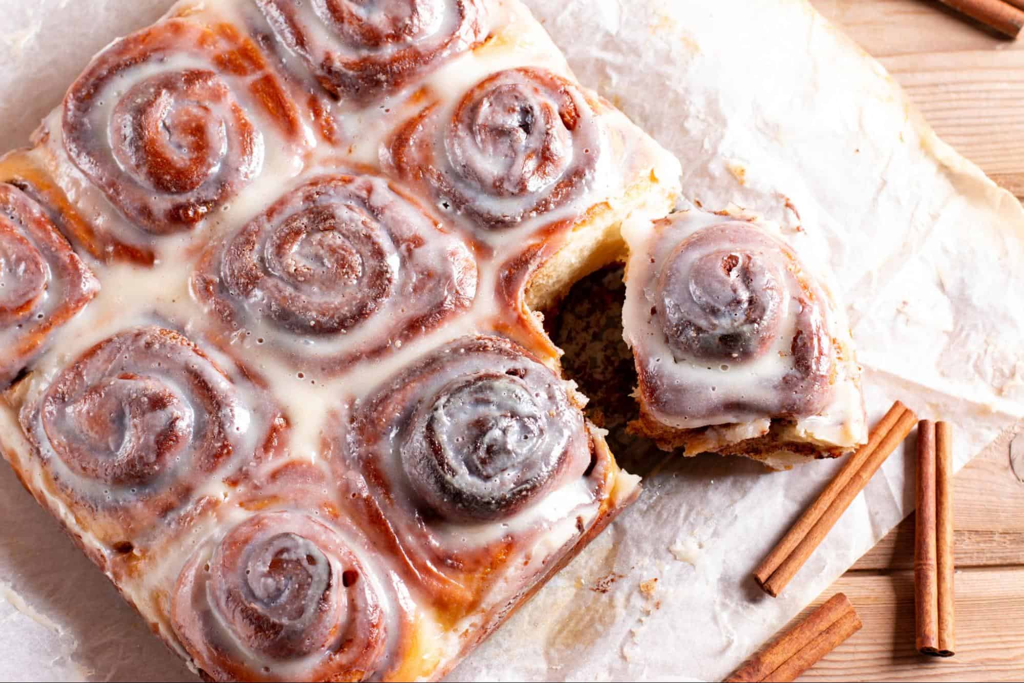 Delicious cinnamon roll cake with cream cheese glaze on parchment paper. Perfect for breakfast or dessert.