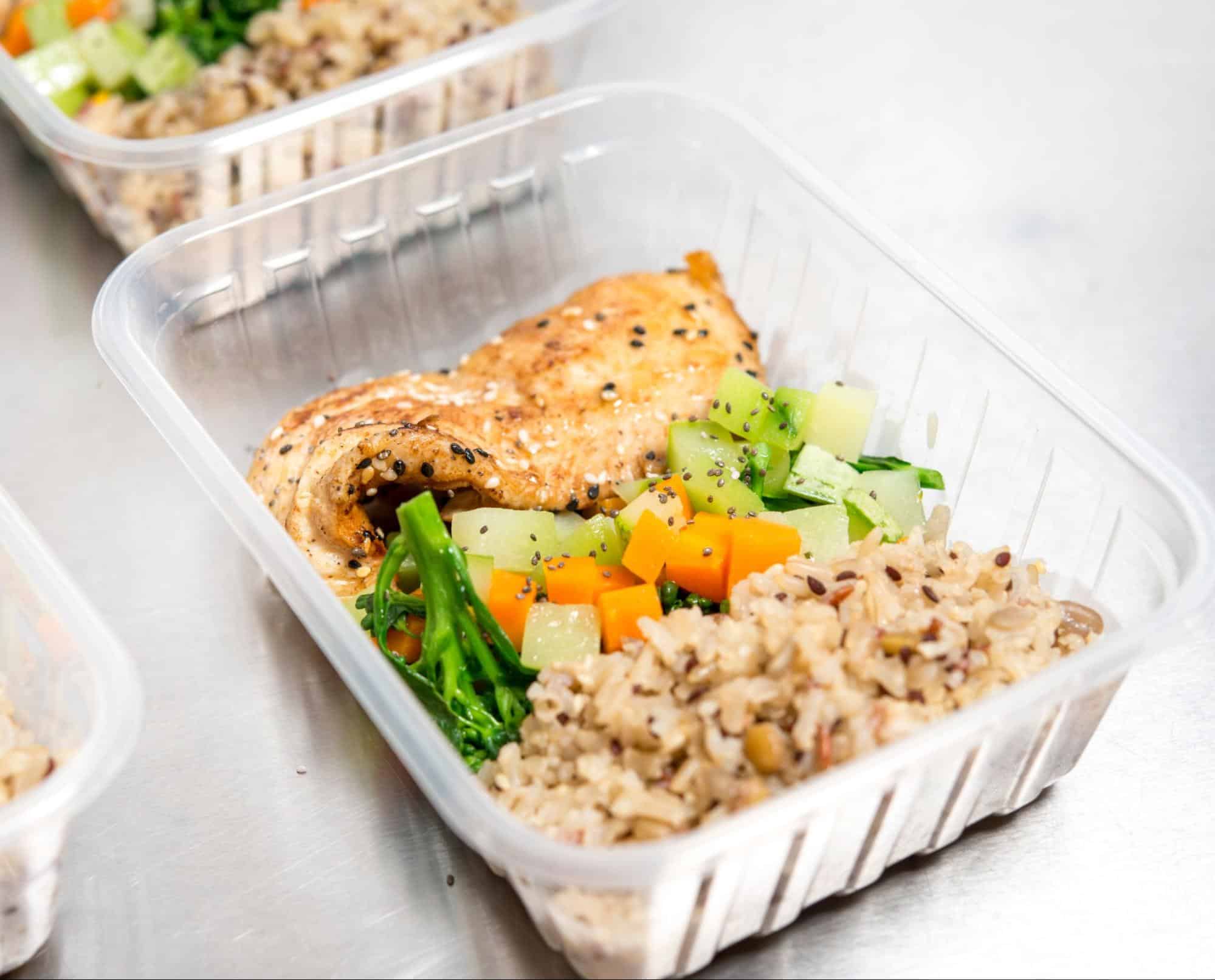 Dog food meal with grilled chicken, mixed vegetables, and rice in a clear plastic container for pets.