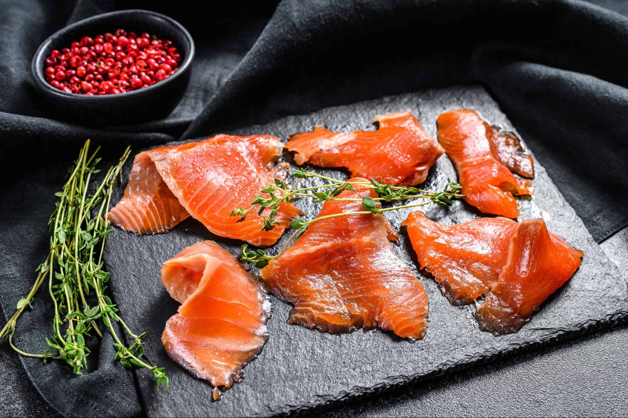 Fresh salmon slices with herbs on slate.