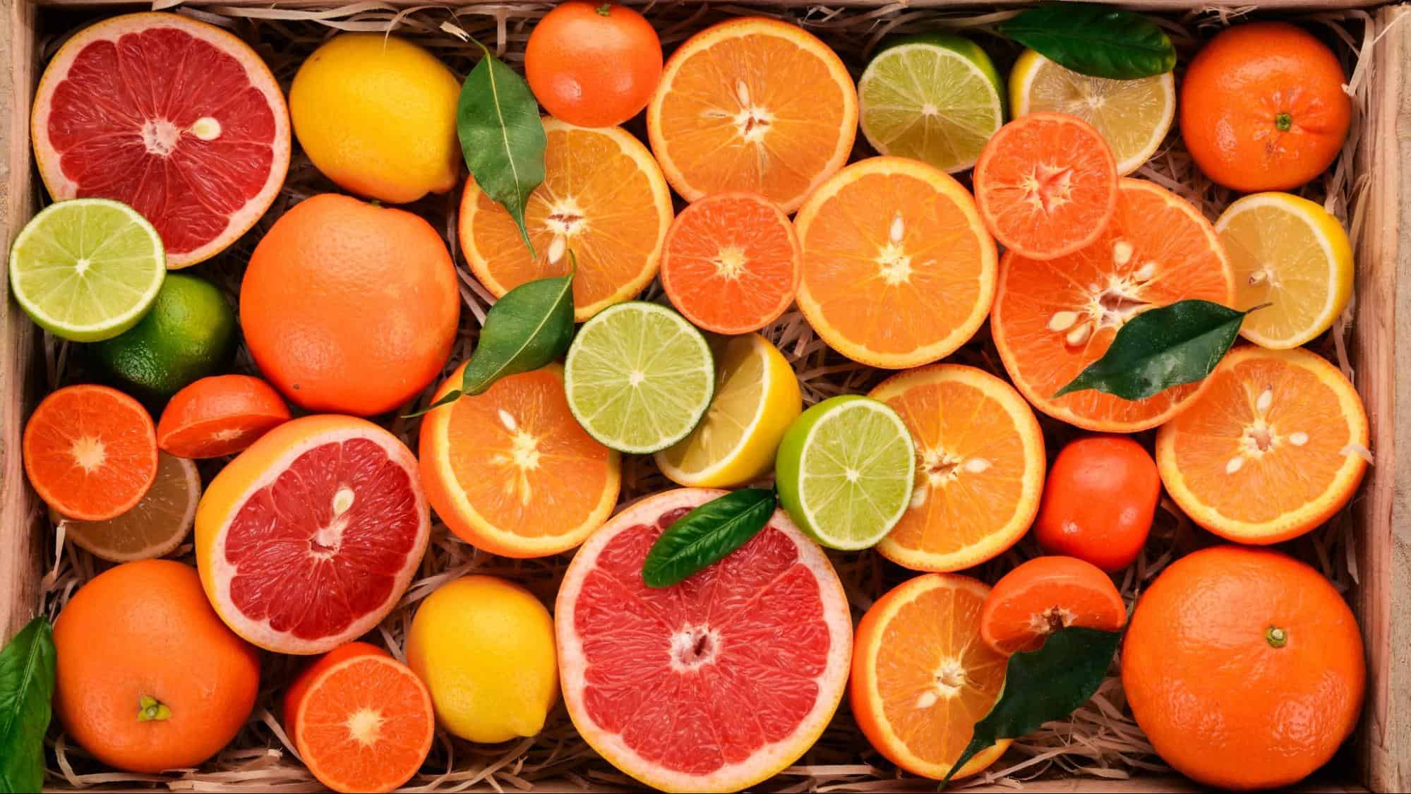 Colorful assorted citrus fruits including grapefruits, oranges, lemons, and limes with green leaves on a rustic wooden background.