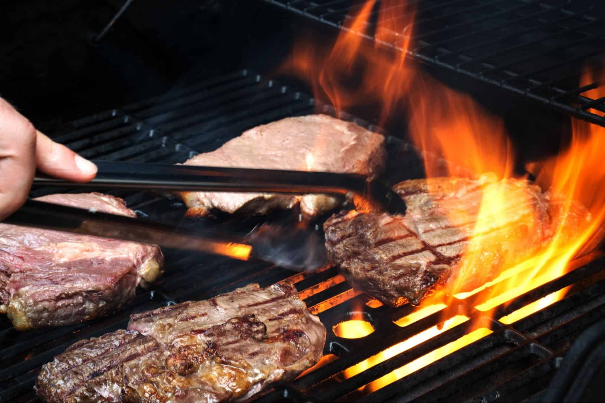 Close-up of delicious steaks being grilled over open flame on barbecue. Perfect for outdoor cooking and summer BBQs.