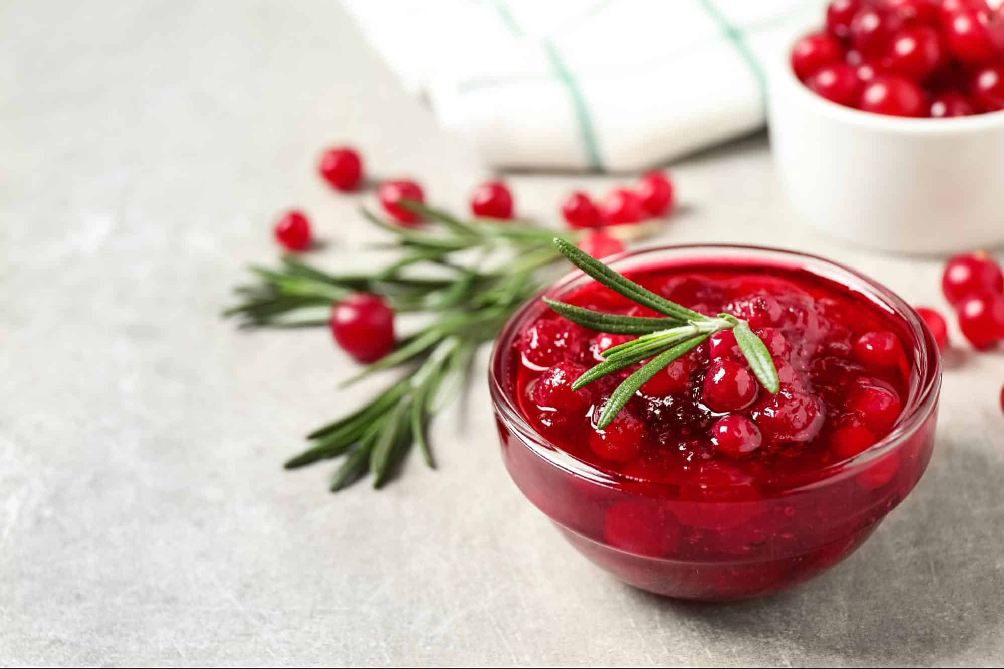 Fresh red berry jam in a glass bowl with rosemary garnish.