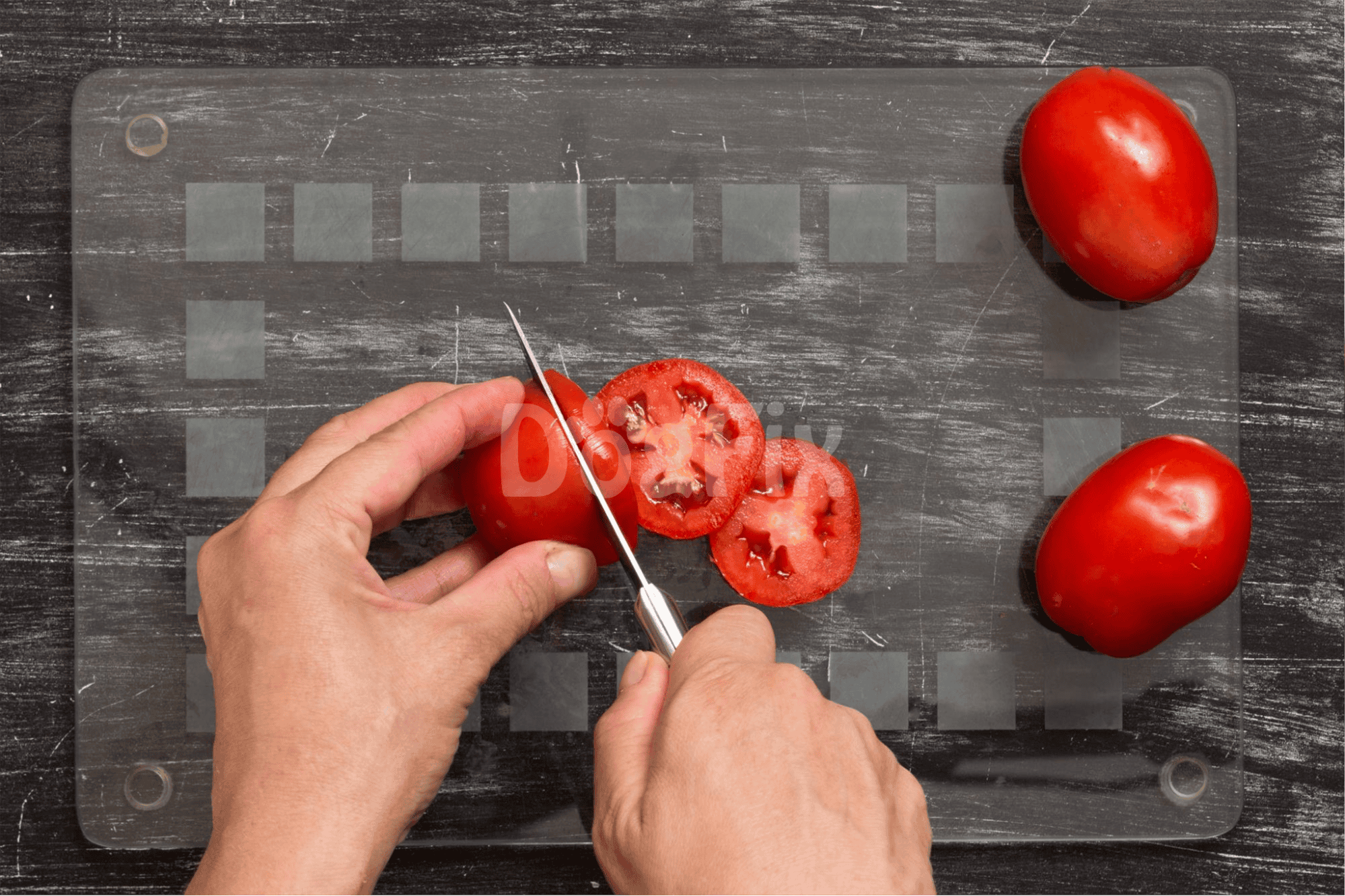 Close-up of hands slicing ripe tomatoes on a glass cutting board for nutritious dog snacks.