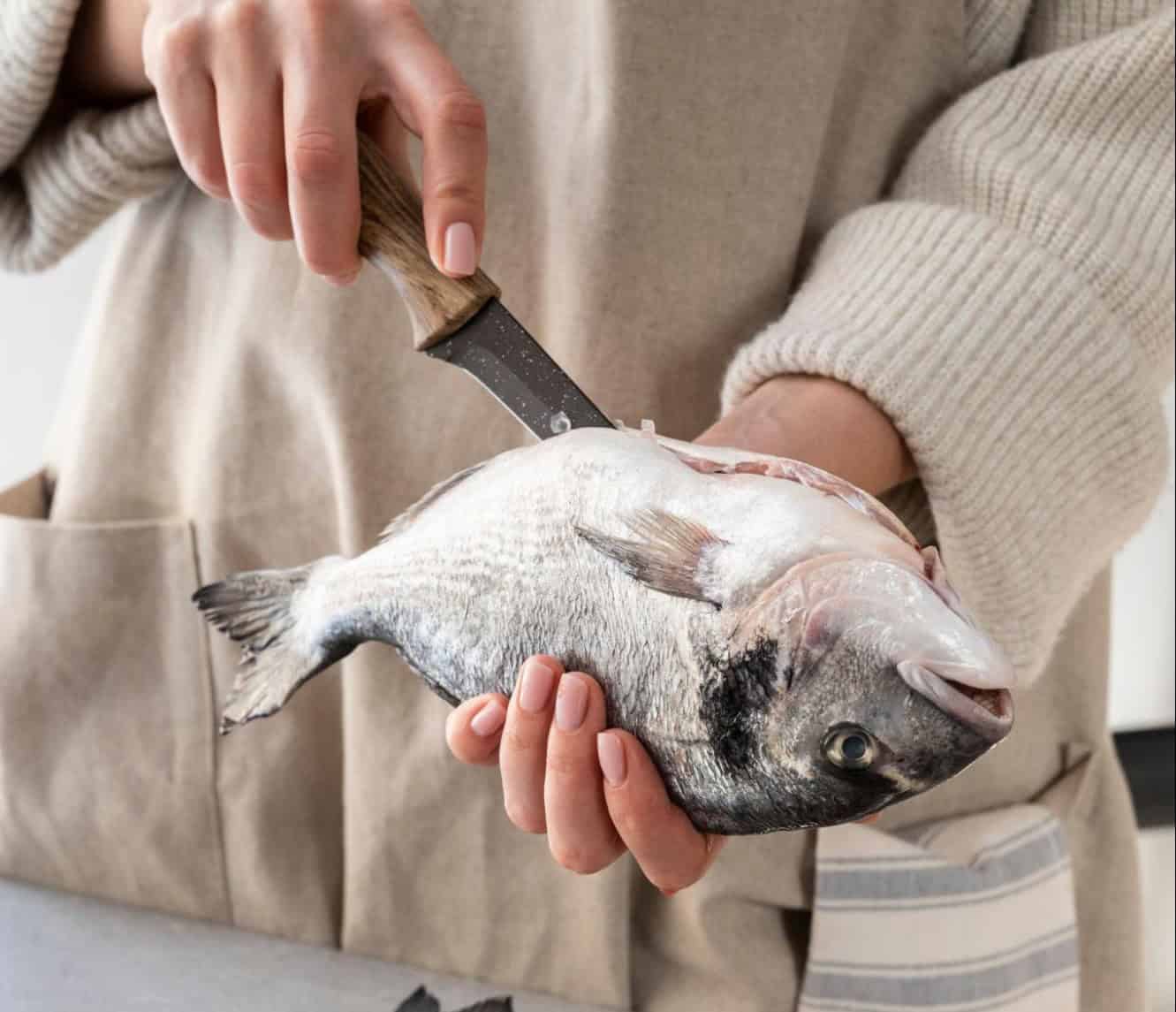 Photo of a person holding a fish and using a knife, related to pet nutrition and fish-based dog food.