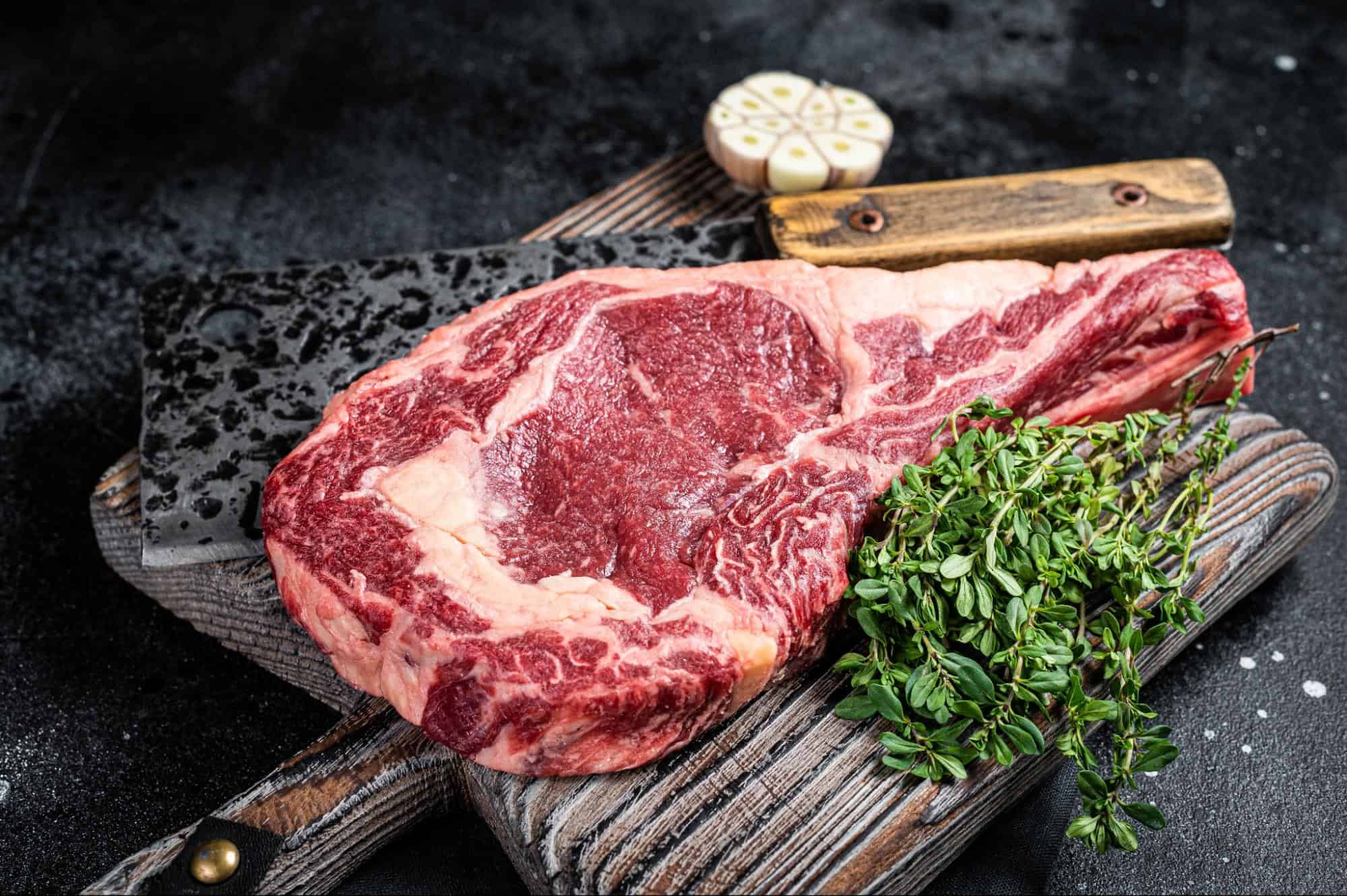 High-quality marbled beef steak on rustic cutting board with fresh herbs and garlic. Perfect for grilling or fine dining.