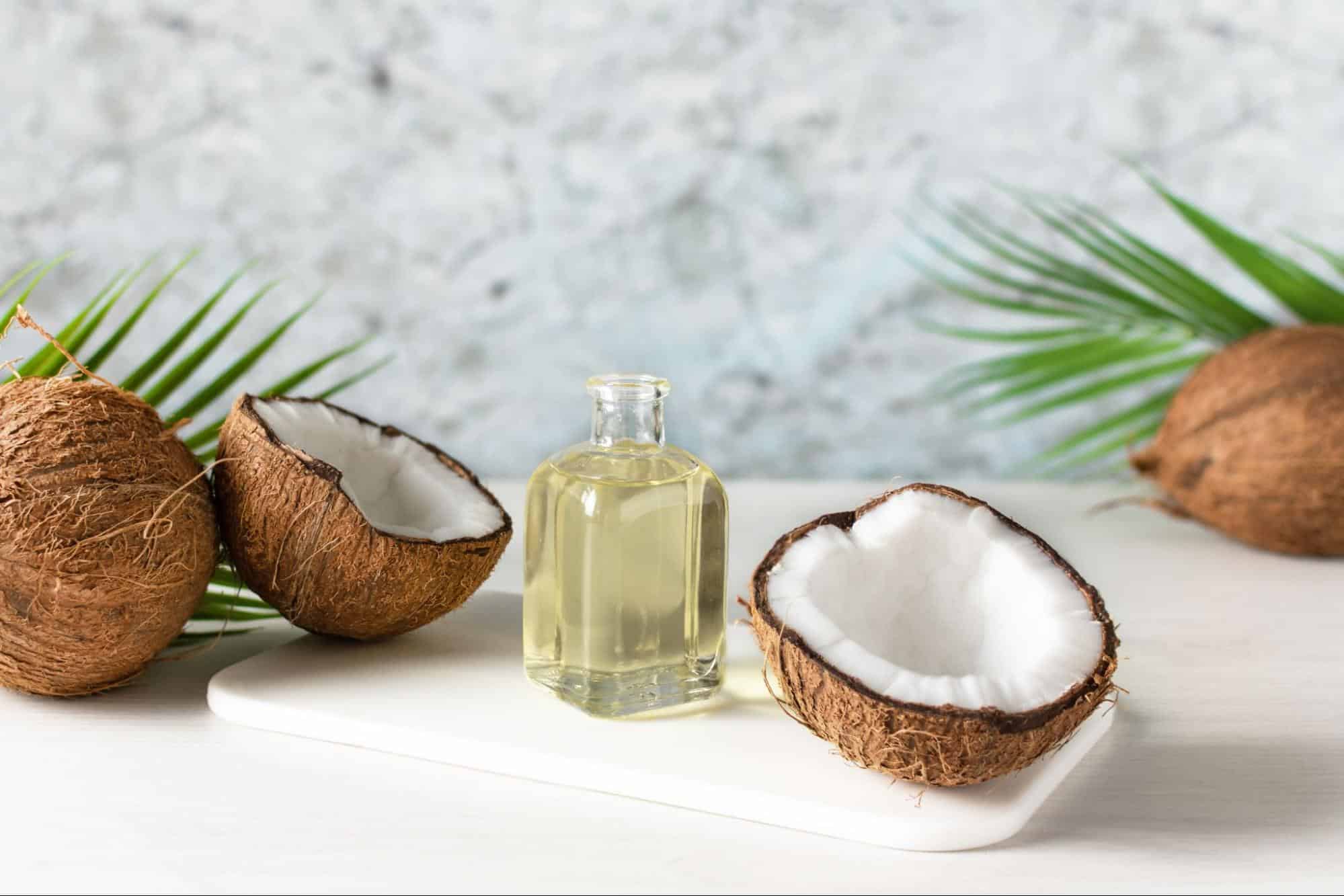 Natural coconut oil in a glass bottle with coconut halves on a white background.
