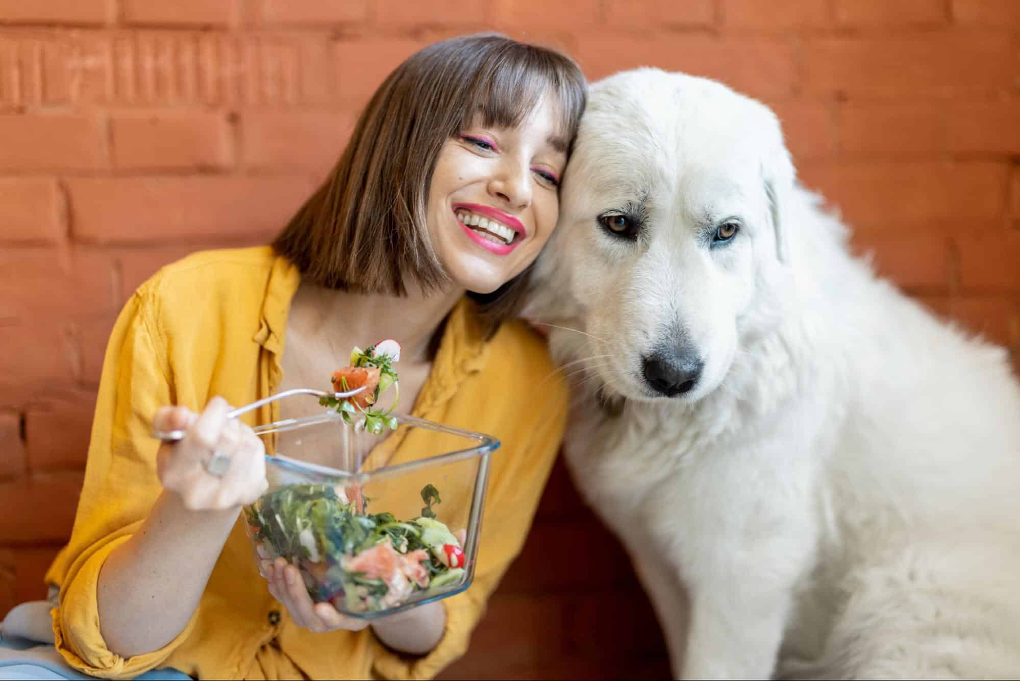 Happy woman with a big smile enjoying a fresh salad with her adorable dog.