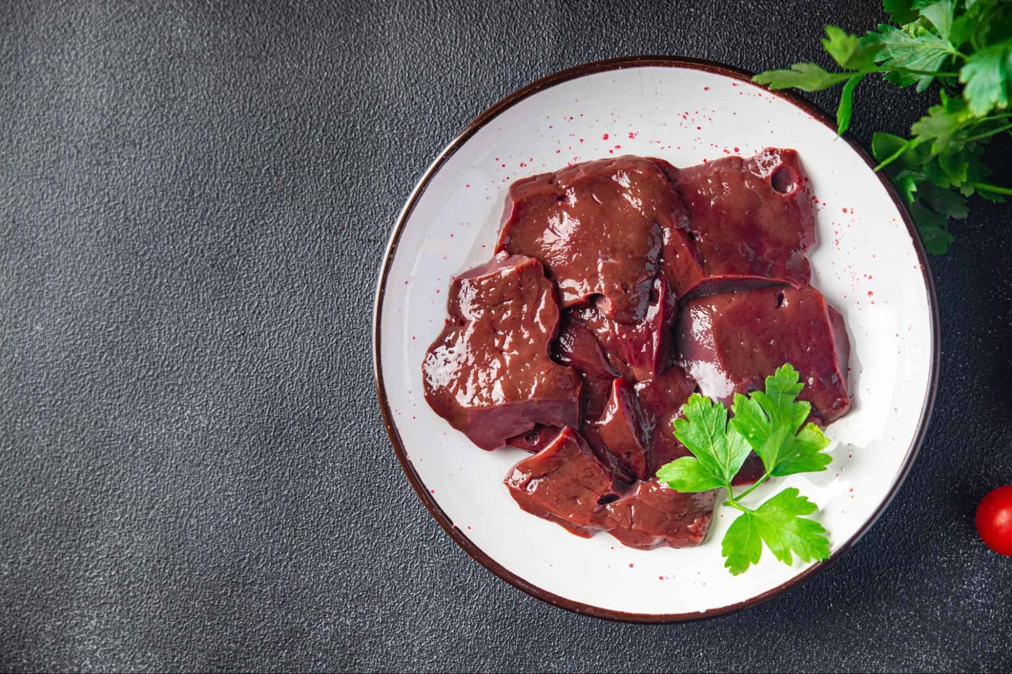 Dog-friendly raw liver meat on a white plate with fresh herbs, suitable for canine nutrition.