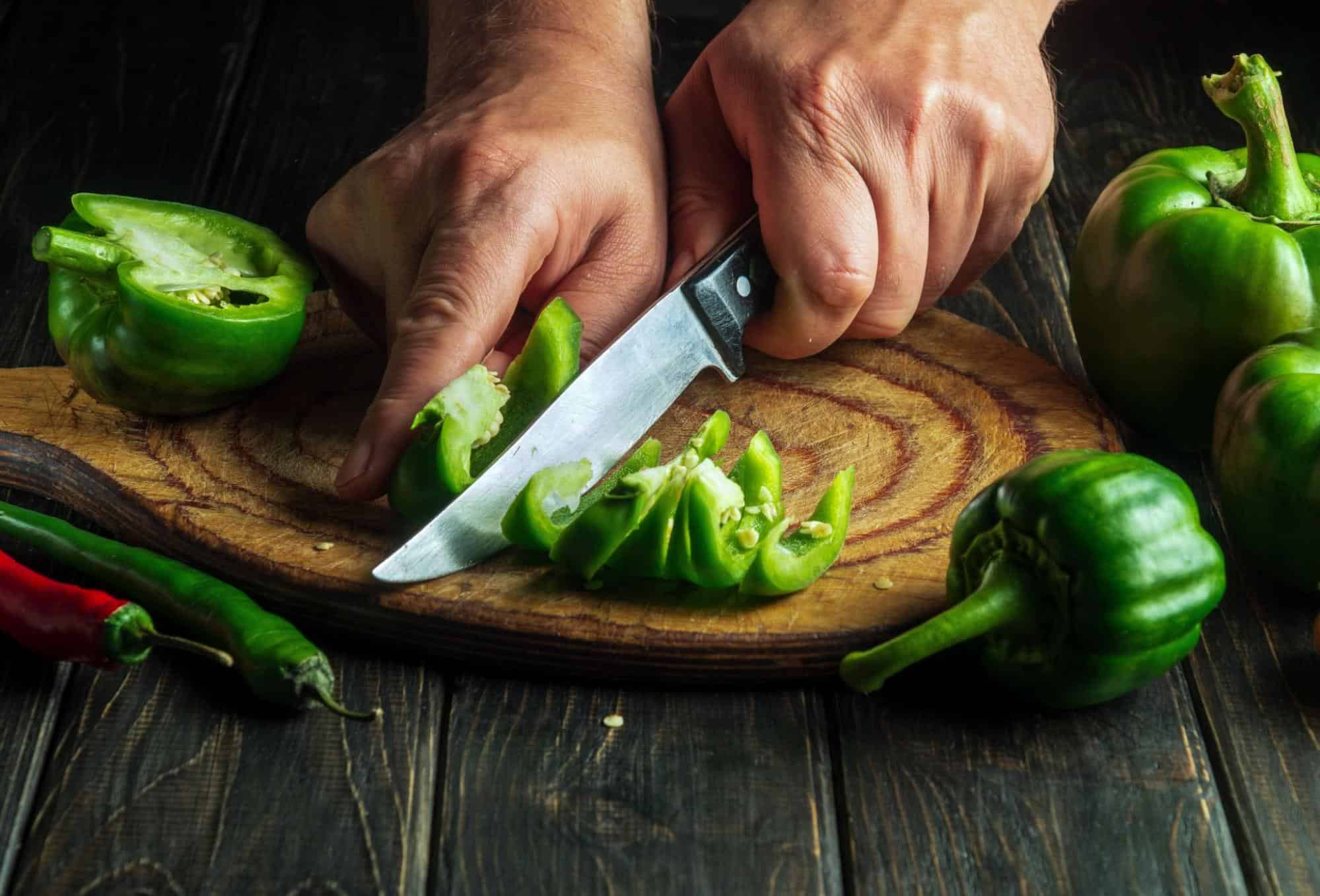 Close-up of hands slicing green peppers for nutritious homemade dog food.