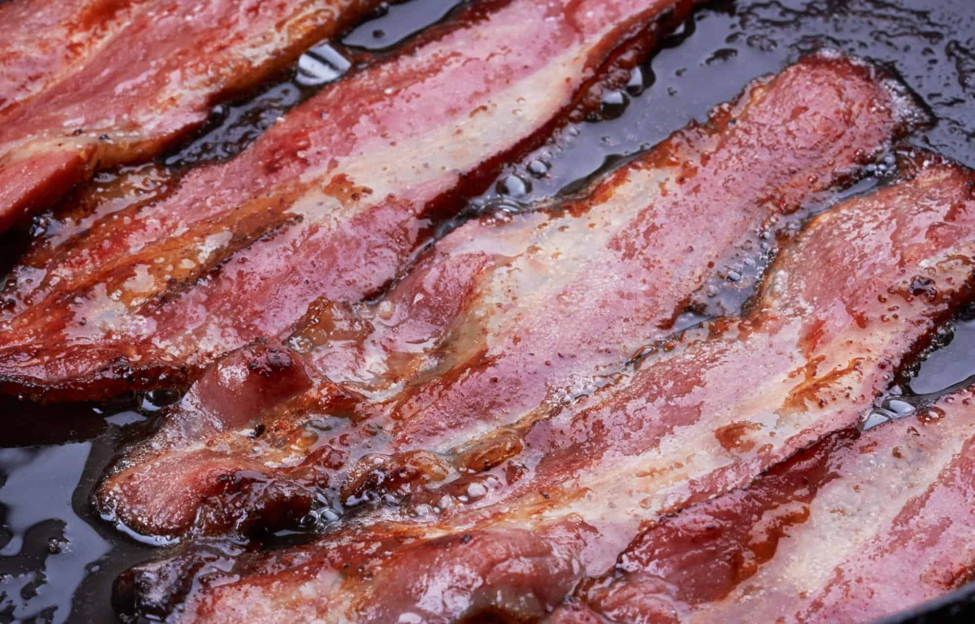Close-up of crispy bacon strips cooking in sizzling oil.