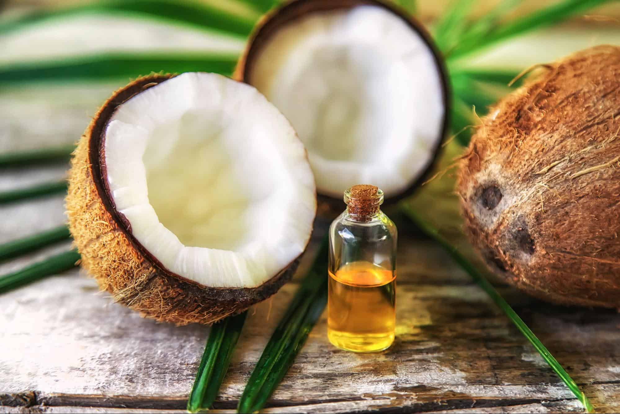 Natural coconut oil in a glass bottle with coconut halves on a white background.