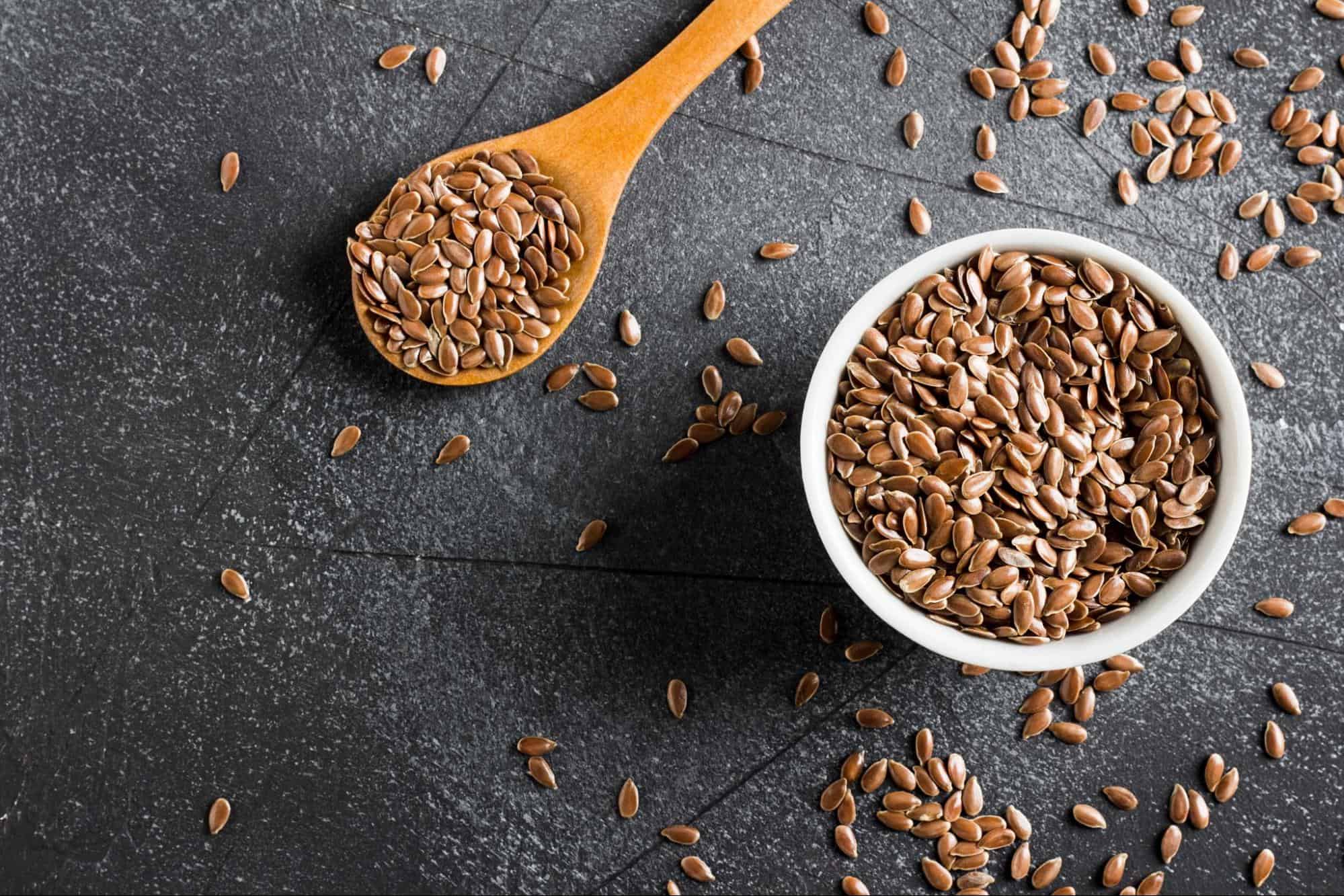 Flaxseed in a white bowl and on a wooden spoon, healthy omega-3 supplement for dogs.