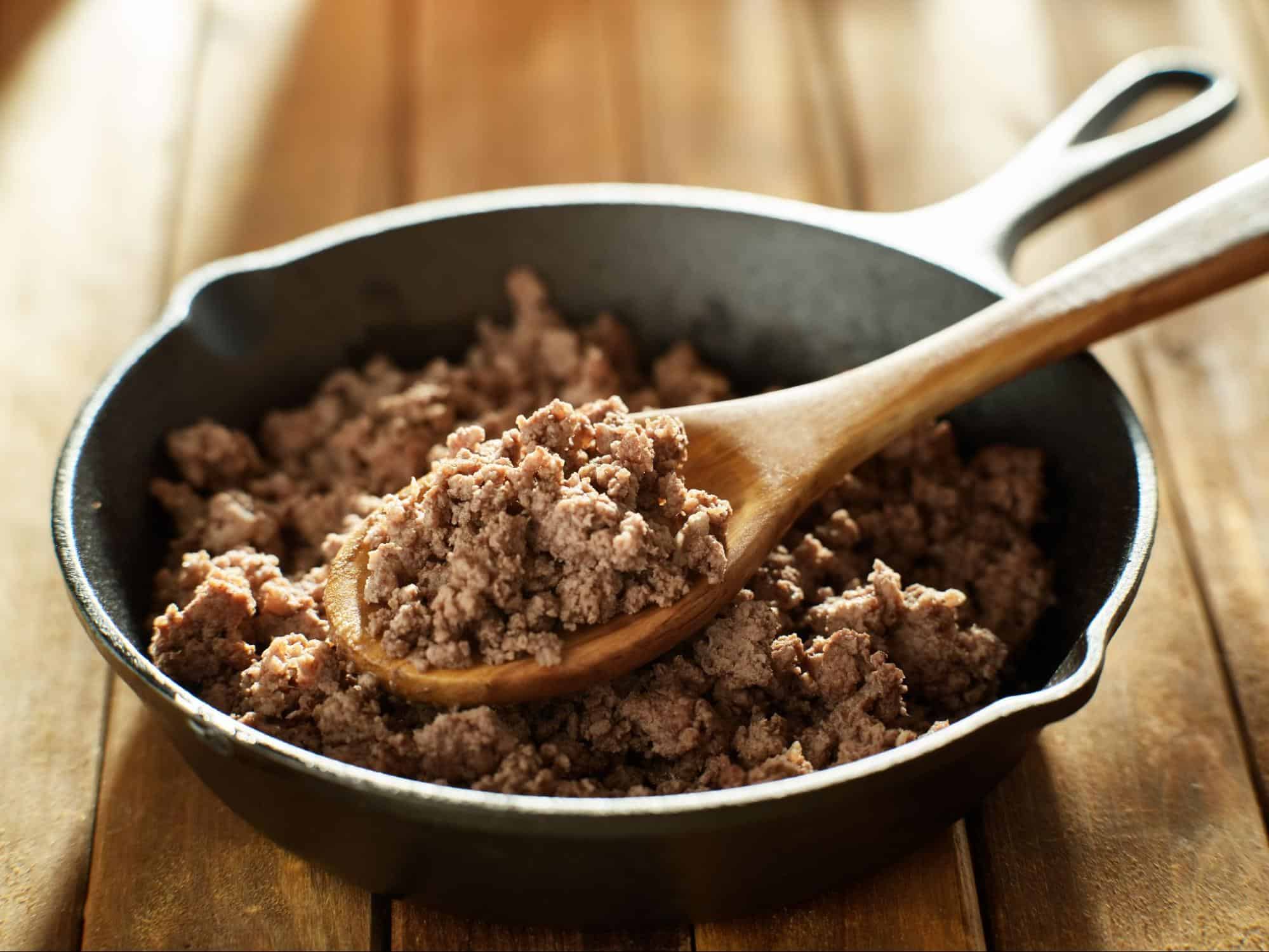 Delicious cooked ground beef in a skillet with a wooden spoon, perfect for dog food recipes and pet nutrition.