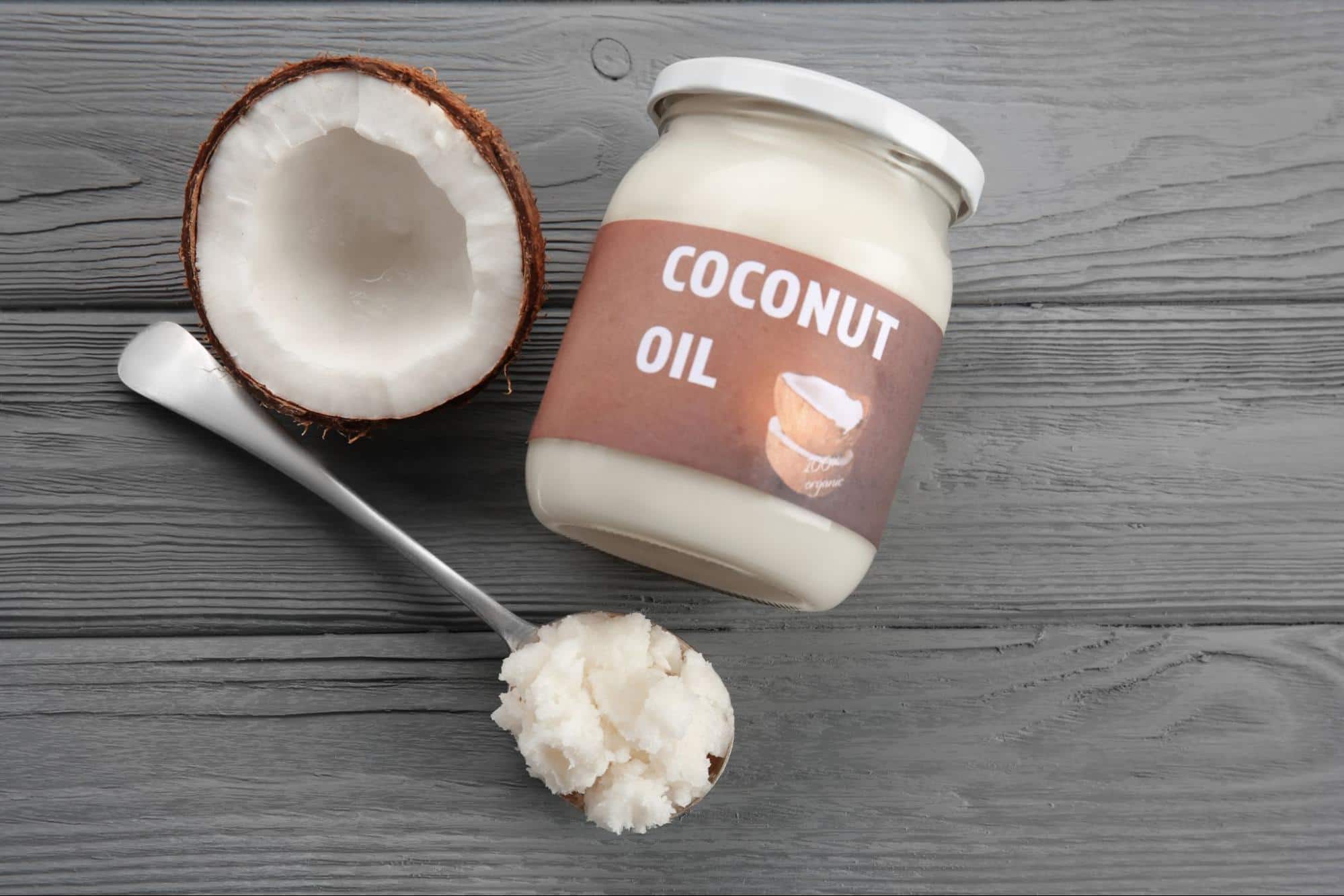 Natural coconut oil in a glass bottle with coconut halves on a white background.
