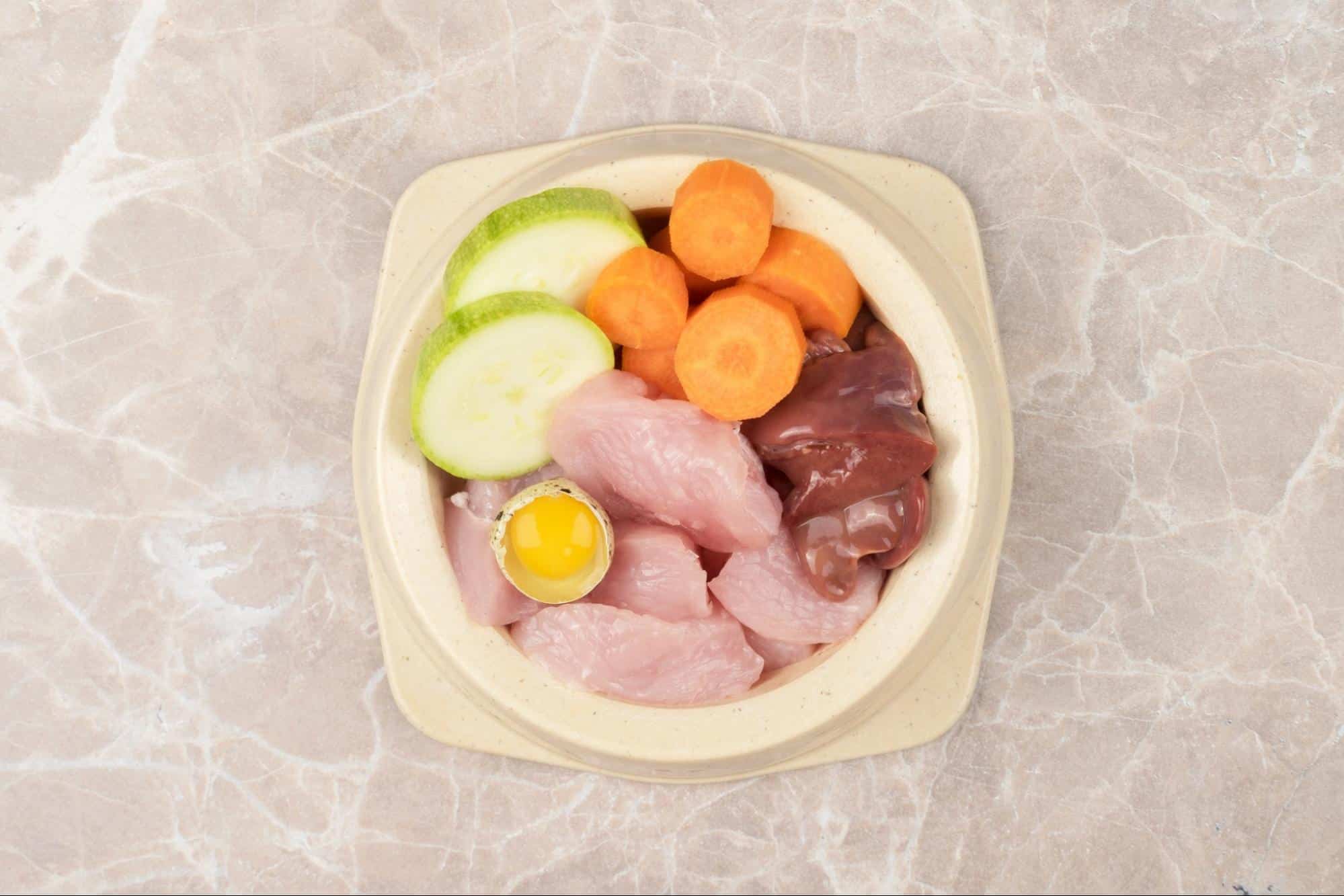Healthy dog food ingredients: chicken, liver, egg, cucumber, carrots for nutritious pet meals.