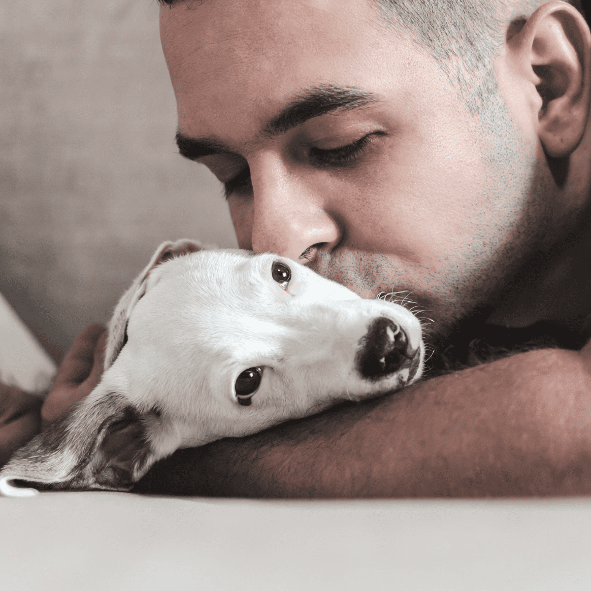 Close-up of a man cuddling a small white puppy.