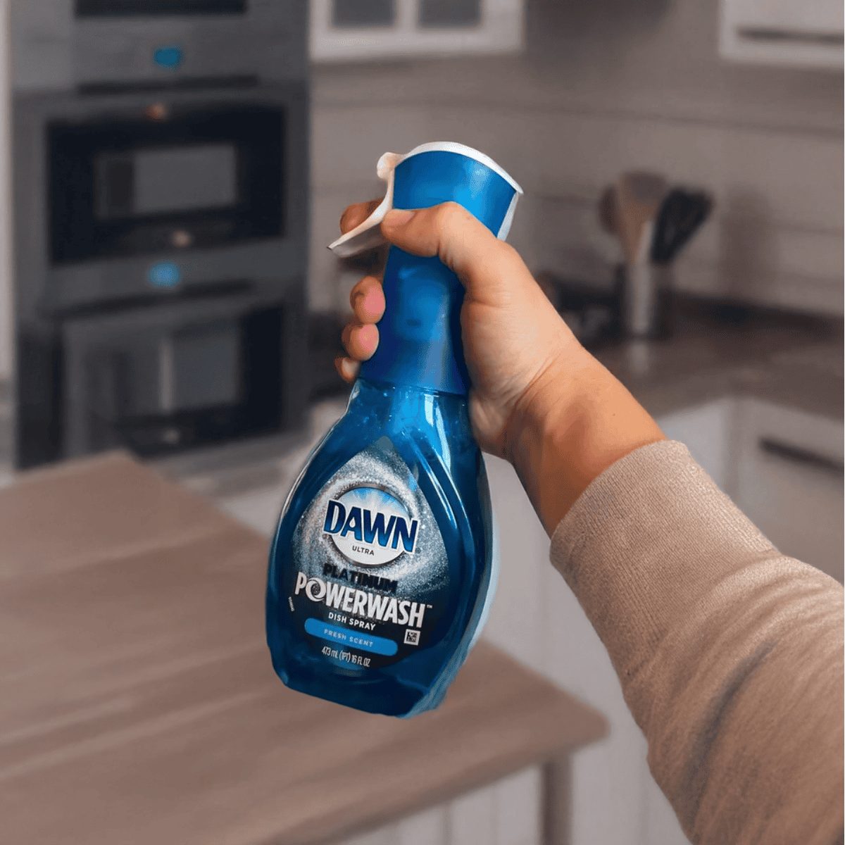 Alt text: Hand holding Dawn Powerwash dish spray bottle in kitchen background.