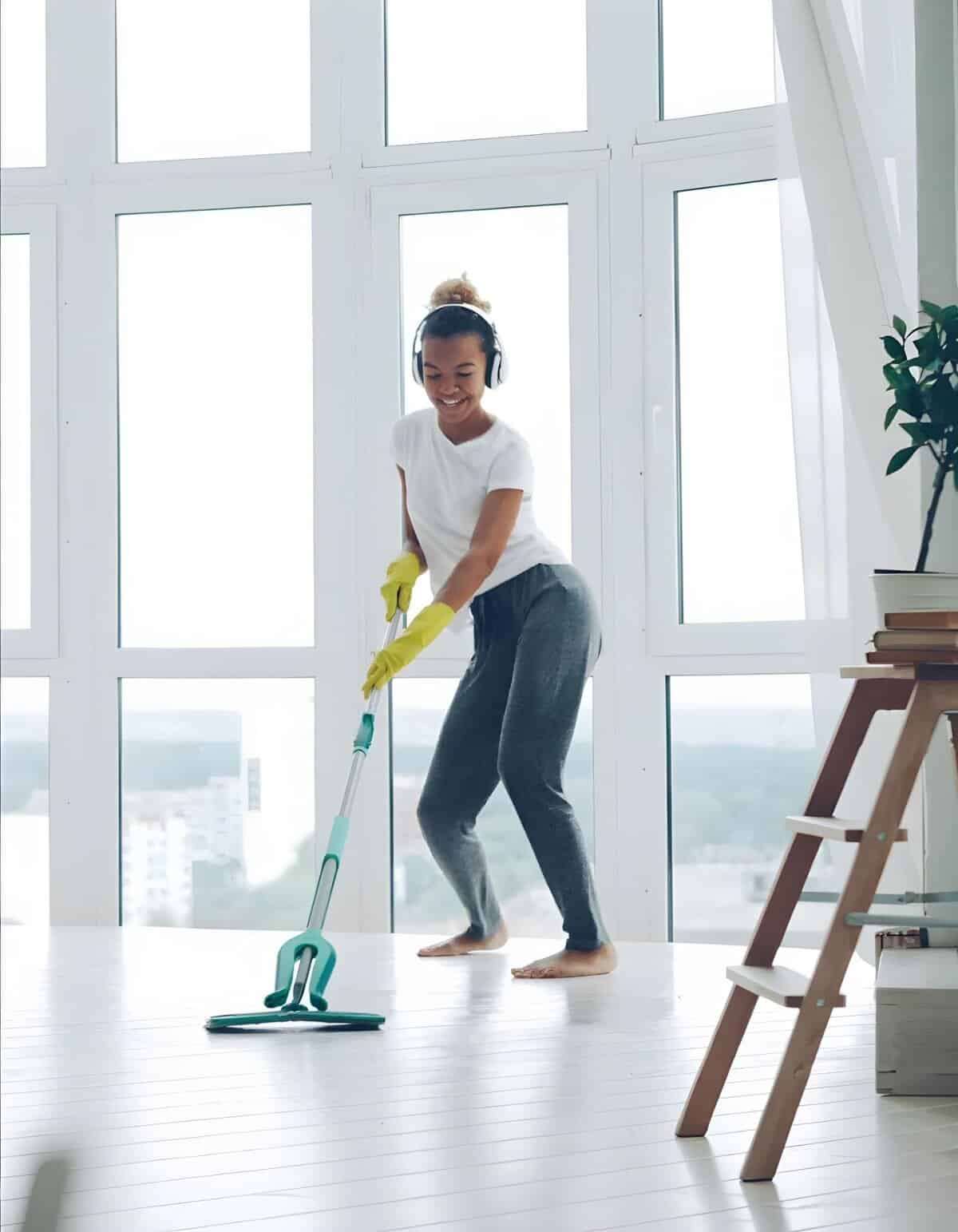 Happy woman cleaning hardwood floor with mop.