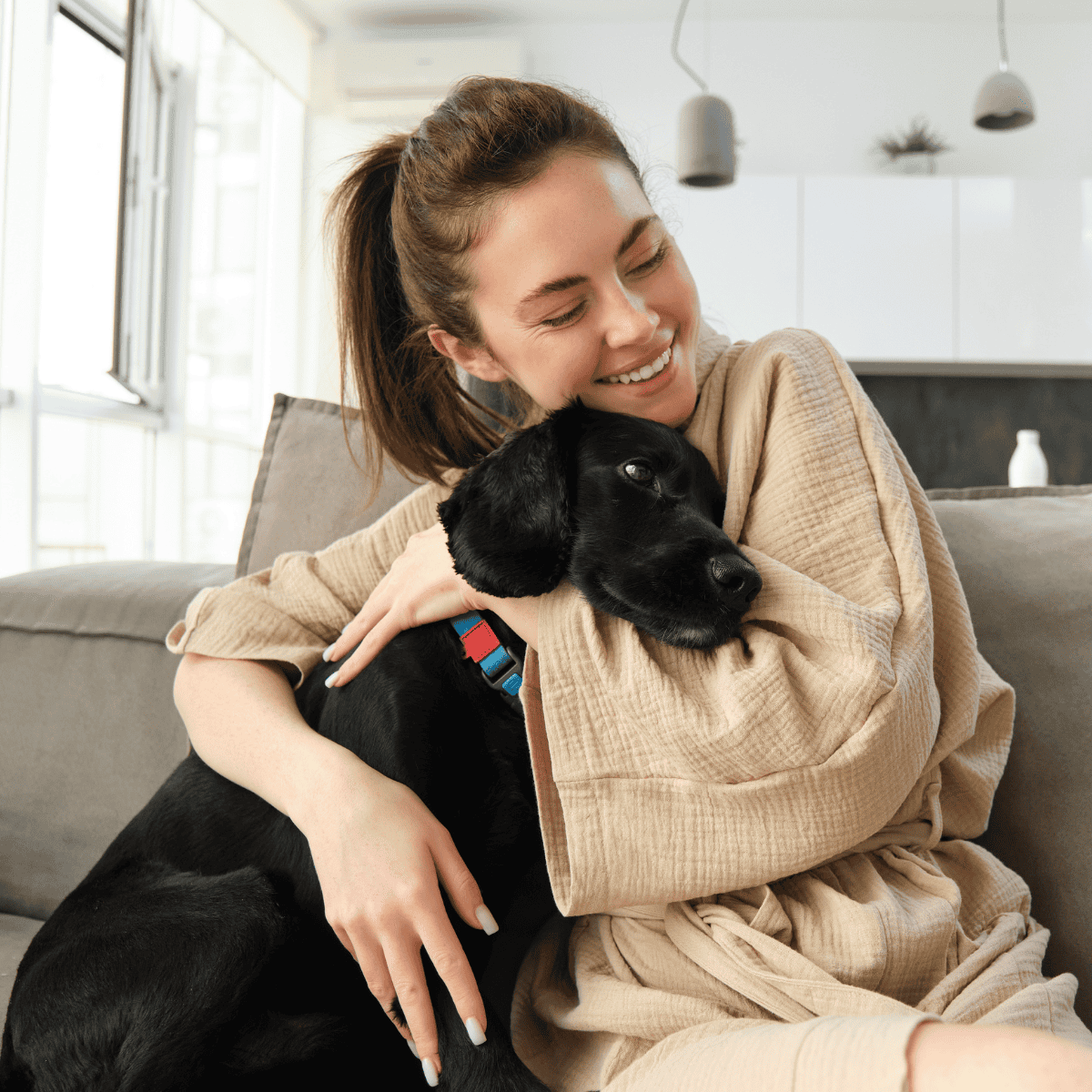 Cute black Labrador puppy cuddling with young woman at home.