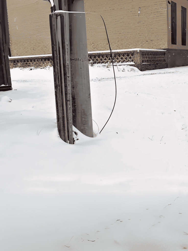 Electrical wire tangled around a pole with snow-covered ground.