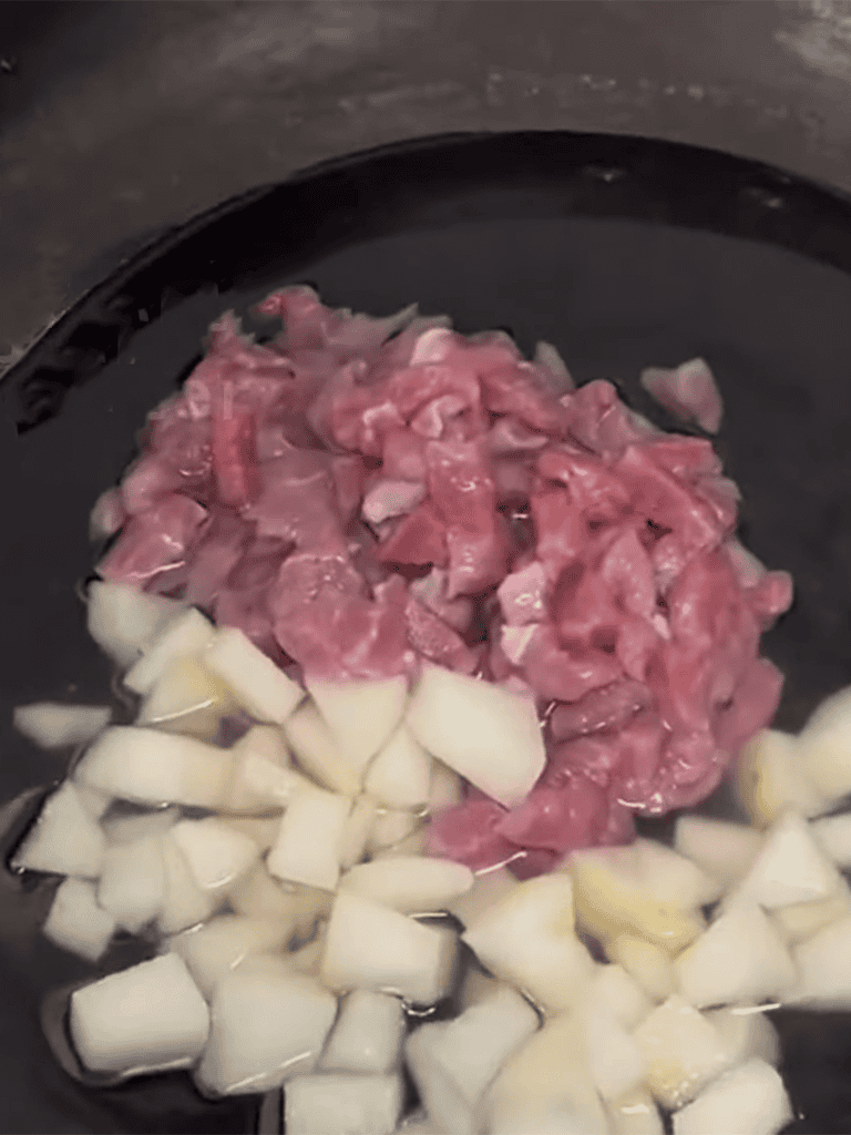 Delicious raw steak and chopped onions sizzling in a black frying pan.